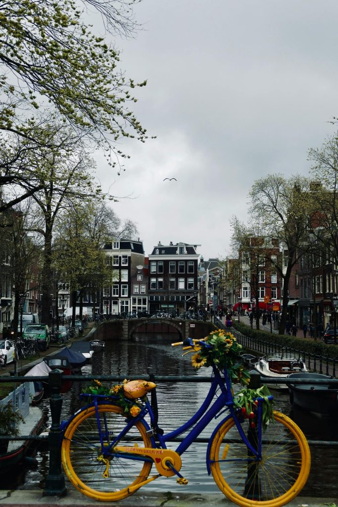 Vibrant bicycle adorned with flowers on a bridge over Amsterdam's iconic canals.