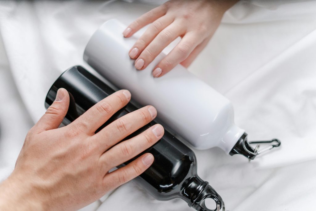 Close-up of hands holding reusable black and white tumblers on a white surface.